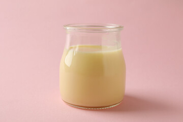 Glass jar with condensed milk on pink background