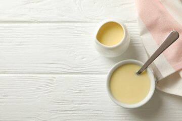 Kitchen towel and bowls with condensed milk on wooden background