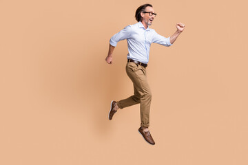 Fototapeta na wymiar Full length profile photo of guy jump run excited wear eyewear shirt pants shoes isolated beige color background