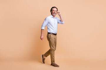 Full length photo of man step fingers hold eyewear wear specs shirt pants shoes isolated beige color background