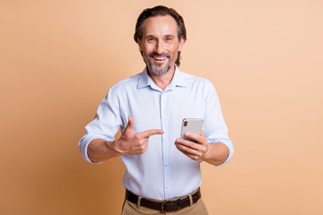 Photo of bearded man hold smartphone indicate forefinger look camera wear shirt isolated beige...