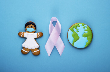 pink ribbon and gingerbread girl and planet earth on blue background. world day of fight against cancer