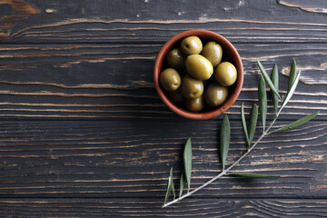 Green olives with a pit in a bowl on a wooden background. Space for text. Olive Tree. Olive branch.