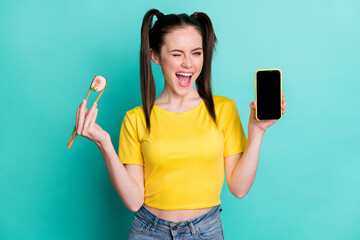 Photo of adorable young lady wear yellow crop top holding maki roll modern gadget winking isolated...