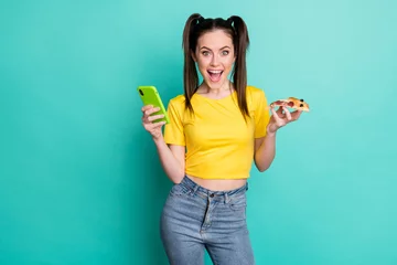 Foto op Plexiglas Photo of excited funny young woman dressed yellow t-shirt holding modern gadget pizza isolated teal color background © deagreez