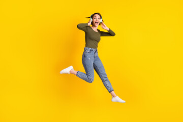 Full size photo of crazy girl jump listen music on headset wear sweater isolated over shine yellow color background