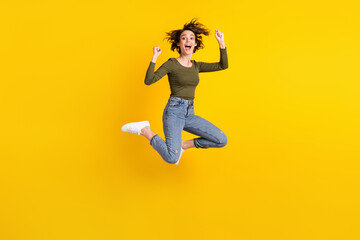 Fototapeta na wymiar Full length photo of ecstatic girl jump raise fists wear sweater gumshoes isolated on shine yellow color background