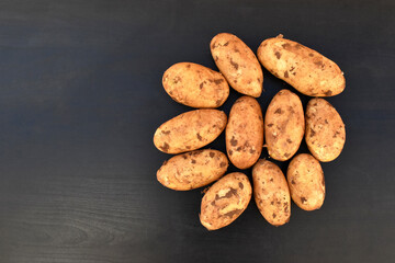 Fototapeta na wymiar Raw potatoes on black wood table. Copy space is on the left side. 
