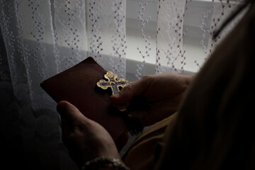 Close up of woman hands praying by the window. Praying hands holding cross and praying book