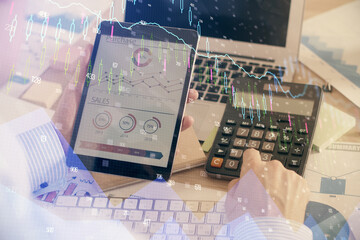 Double exposure of man's hands holding and using a digital device and forex graph drawing. Financial market concept.