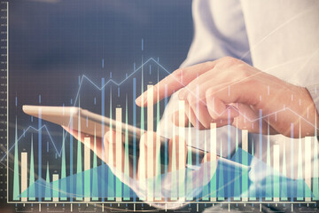 Double exposure of man's hands holding and using a digital device and forex graph drawing. Financial market concept.