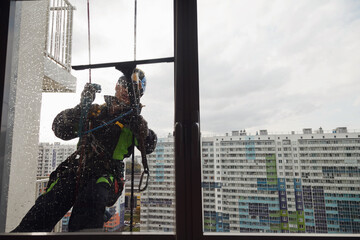 Industrial mountaineering worker hangs over residential building while washing exterior facade glazing. Rope access laborer hangs on wall of house. Concept of urban works. Copy space