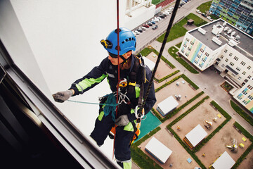 Industrial mountaineering worker hangs over residential building while washing exterior facade...