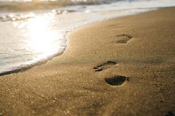 Fototapeta na wymiar Footprints in the sand at sunset. Beautiful sandy tropical beach with sea waves