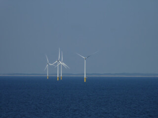 Offshore Windenergieanlagen im Meer. Erneuerbare Energien. Tiefe blaue Landschaftmit weißen Türmen mit gelbem Sockel. Renewable Energie. Verspargeltes Meer verspargelte Landschaft Energiewende concept