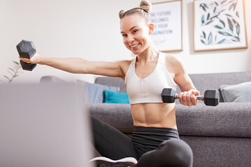 Fototapeta na wymiar Slim woman exercising with dumbbells during online workout