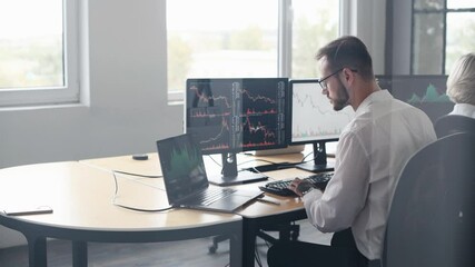 Rear view of male and female stockbrokers in formal clothes that works in the office with financial market and graphs on monitors.