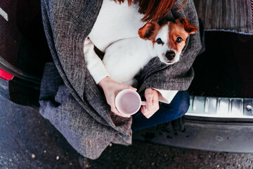 young woman and cute jack russel dog in car. Winter season, snowy mountain background
