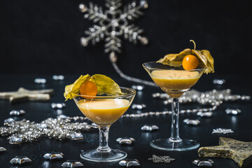 Two glasses with eggnog and physalis fruits on a black background, decorated with silver stars