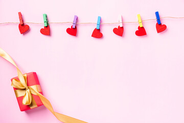Happy Valentine's day concept. red heart-shaped valentines decoration hanging with wood clips for love and red gift box with golden ribbon on the rope isolated on pink background with copy space