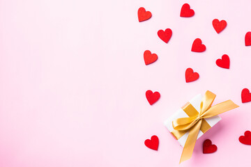 Happy Valentines' day background concept. White gift box with a golden bow ribbon and wood red hearts composition for love isolated on pink background with copy space. Top View from above
