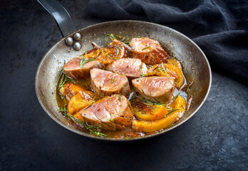 Traditional fried pork filet medaillons in with orange slices and herbs offered as top view in a rustic wrought iron skillet