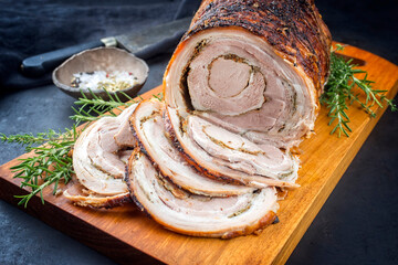 Traditional Italian Porchetta arrotolata pork meat sliced and as piece with crust offered as...