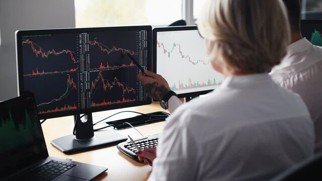 Male and female stockbrokers in formal clothes works in the office with financial market and graphs on monitors and analyzing data.