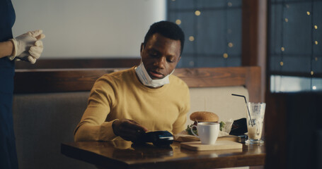 Black man in medical mask paying with card for cafe meal