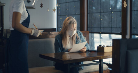 Woman wearing mask and talking to waitress in cafe