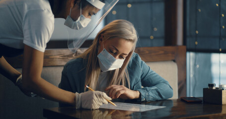 Woman putting on mask visiting cafe during pandemic