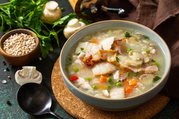 Healthy eating. Homemade hearty soup with cereals, bacon and mushrooms on a dark stone background.