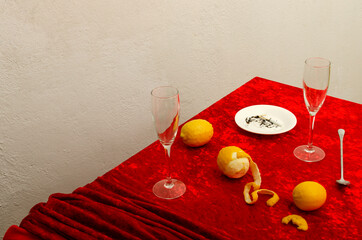 Red tablecloth and glasses, lemons, spoon on the table against white wall.Empty space
