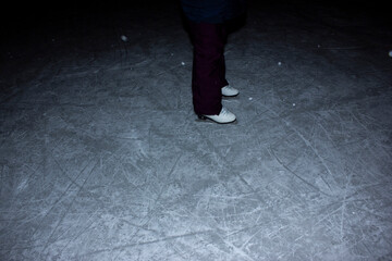 Young woman ice skating outdoors on a pond on a freezing winter day at night - detail of the...