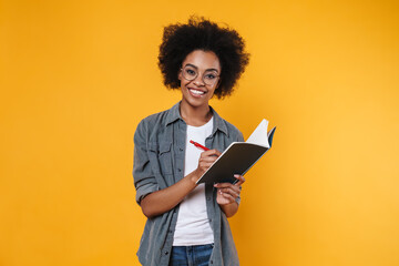 Joyful african american girl in eyeglasses writing in exercise book