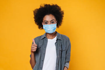 Pleased african american girl in face mask showing thumb up