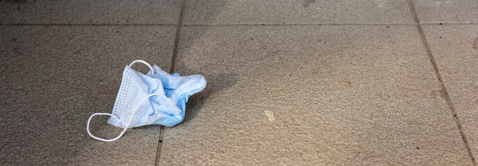 Used lost protective medical face mask on the street stairs. Disposable face mask lying on pavement. Environmental pollution due to the flu pandemic. Banner.