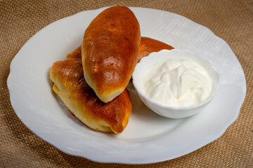 Russian bakery pirozhki (stuffed buns) on white plate with sour cream. Top view
