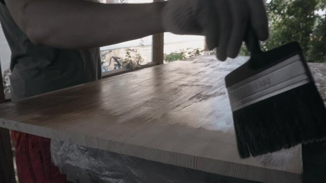 Young man in work uniform and gloves covers the wooden tabletop