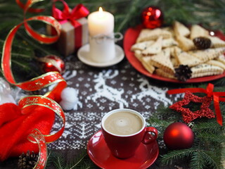 A cup of hot coffee with homemade shortbread cookies and red Christmas decor on a knitted knitted background with deer. Selective focus.Christmas background.Christmas background.