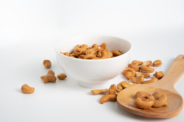 isoloated roasted cashew nuts in white crockery and wooden spoon