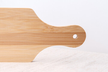 Kitchen cutting board with a hole in the handle. A wooden object stands upside down. The table is covered with a rough light cloth on a gray background.