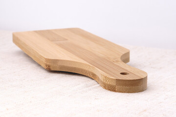 Kitchen cutting board glued from slats. The subject lies diagonally and casts a shadow. The table is covered with a light textured fabric against a gray wall.