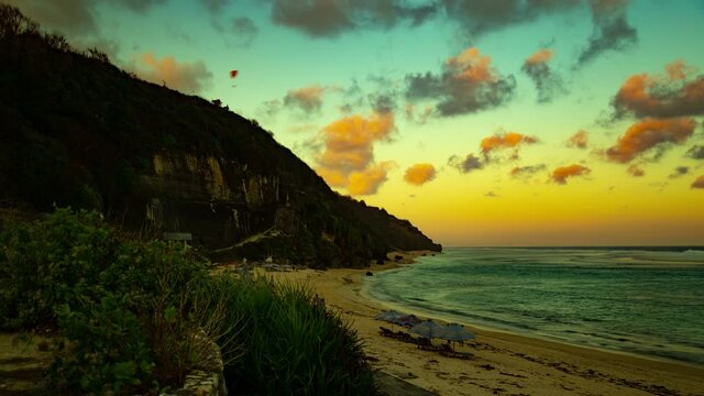 Paragliders fly during a beautiful sunset over the ocean and beach in Bali, Indonesia.