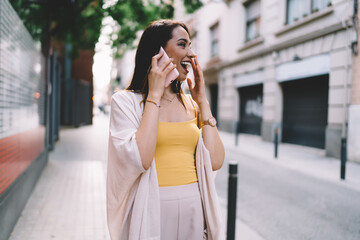 Toothy hipster girl with perfect candid smile on face laughing at urban street satisfied with roaming internet connection, cheerful female tourist rejoicing and feeling delight during mobility talking