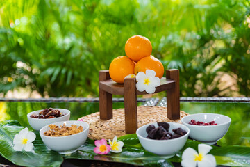 dried fruit ingredients, walnuts on the plate dates cranberries and figs, vegan and vegetarian sweets, oranges on a wooden stand, frangipani flowers for decoration