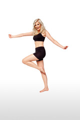 Fototapeta na wymiar Portrait of a joyful fit young white female athlete with curly long blond hair posing by herself in a studio with a white background wearing black shorts & sports bra.