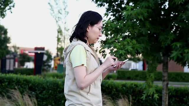 Asian woman walking and reading information on a cellphone