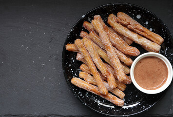 homemade Spanish caramel sugar churros on the black stone table are served together with the chocolate dipping sauce pastry for the morning breakfast meal in the bakery coffee shop