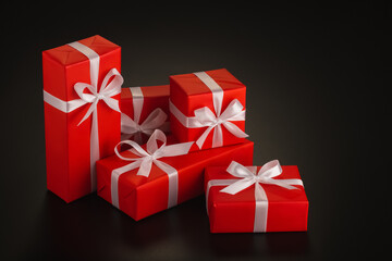Composition of several gifts wrapped in bright red brown paper tied with a white satin ribbon on a black background. Copy space.